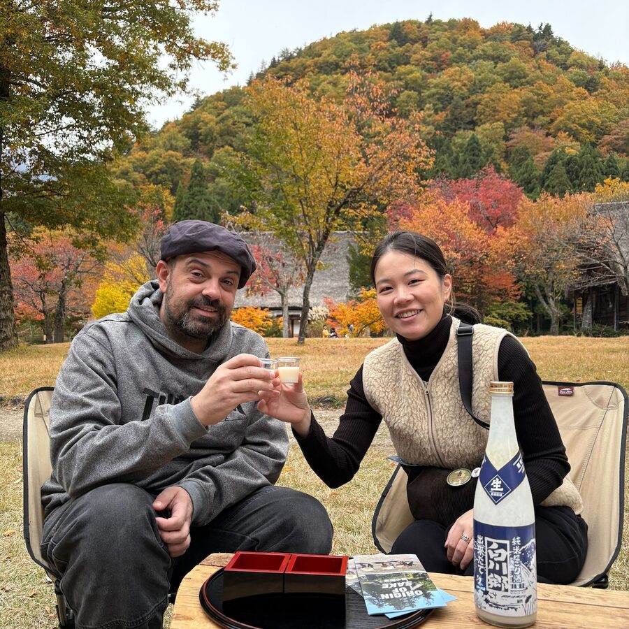 Liam and Marisa toasting with sake before autumn mountains